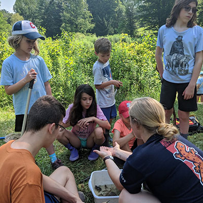 camp counselor shows camp kids a pond creature