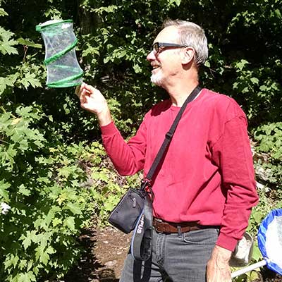 man holding a butterfly net and looking into a netted container to hold butterflies.