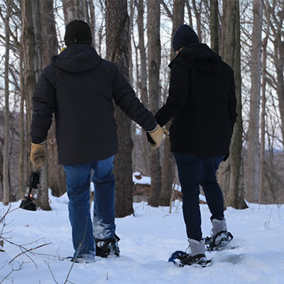 two-snowshoers at Baltimore Woods on a trail carrying an old fashioned kerosene lantern