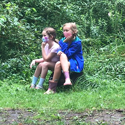 two grsl sittng on a log in a field watching the world go by