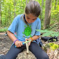 camper whittles a piece of wood starter with a knife