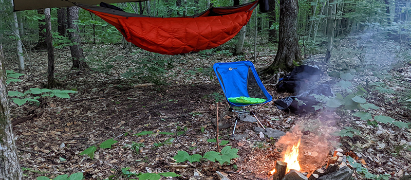 Image of a campground with hammock, fire, and camping chair.