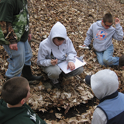 Science Adventures in Nature participants sitting on the forest floor together at Baltimore Woods.