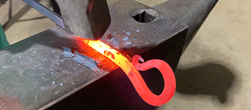 Red hot steel being forged into the shape of a shepherd's crook on an anvil.